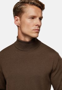 Brown ribbed turtleneck sweater with a fitted design, textured fabric, and a high collar, showcasing a seamless, clean finish.
