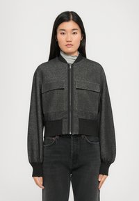 Veste bomber coupée en tissu gris foncé, avec deux poches poitrine, des poignets côtelés et une fermeture éclair à l'avant.