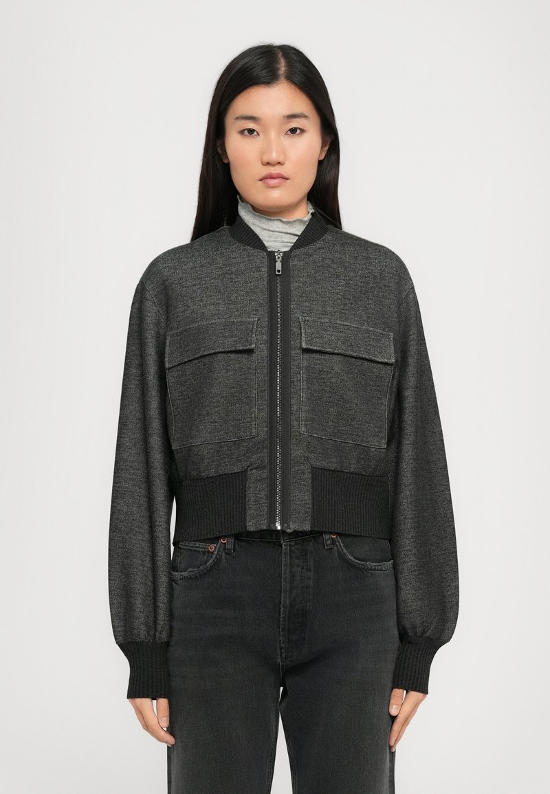 Veste bomber coupée en tissu gris foncé, avec deux poches poitrine, des poignets côtelés et une fermeture éclair à l'avant.