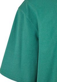 Tricou verde din bumbac, cu mânecă scurtă și guler rotund, cu o textură netedă și linii simple, curate.