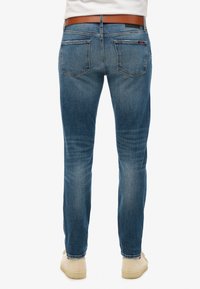 Jeans de mezclilla azules para hombre, corte recto, lavado medio, diseño de cinco bolsillos, cinturilla de cuero, bolsillos traseros visibles, material de algodón.