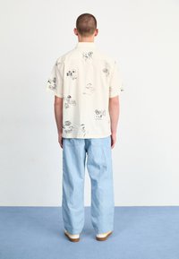 Crème kortemouwen shirt met zwarte gedrukte ontwerpen, gecombineerd met lichtblauwe wijde broek. Casual pasvorm, minimale textuur en eenvoudige details.