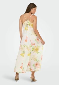 Blommig maxikjol med vit bakgrund, som har gula, rosa och gröna blommor. Justerbara remmar och en knytbakdetalj.