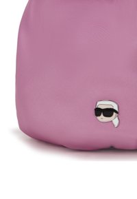 Pink fabric bag corner with a small pin showing a stylized face wearing dark sunglasses and a white headscarf.