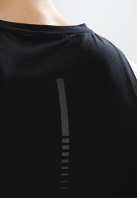 Camiseta sin mangas negra de estilo atlético con una tela texturizada y un detalle de franja reflectante vertical en la parte posterior.