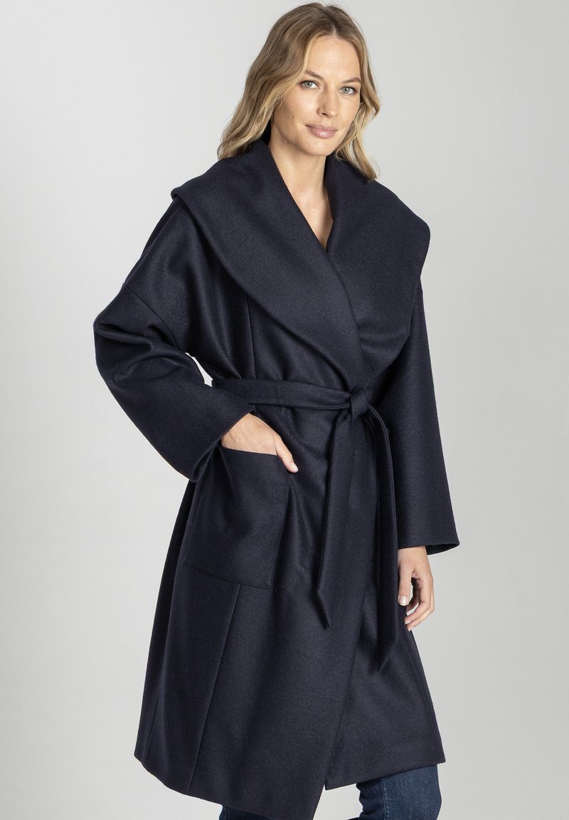 Granatowy płaszcz typu wrap z szerokimi klapami, z paskiem w talii i dwiema przednimi kieszeniami; wykonany z miękkiego materiału o gładkiej teksturze.