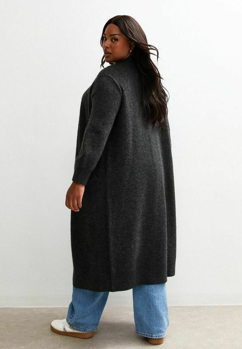Gros cardigan gris foncé en maille douce avec une coupe décontractée, doté de manches longues et de poches latérales, associé à un jean bleu clair.