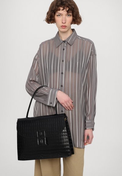 Borsa a tracolla nera in pelle con stampa a coccodrillo, dalla superficie liscia, forma rettangolare e manico superiore, abbinata a una camicia grigia trasparente a righe.