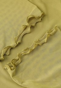 Tkanina w kolorze żółto-zielonym o teksturowanej powierzchni, z dwiema falującymi, przeszytymi falbanami tworzącymi delikatne fałdy na całej powierzchni.