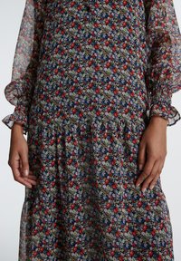 Blumenmuster-Kleid mit Rüschensämlen, das eine Mischung aus roten, blauen und cremefarbenen Blumen auf einem dunklen Hintergrund zeigt. Leichtes, durchsichtiges Material.