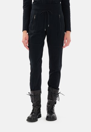 Pantaloni da jogging neri con vita regolabile tramite cordoncino, tasche con zip e dettagli in pannello testurizzato, abbinati a stivali neri con lacci.