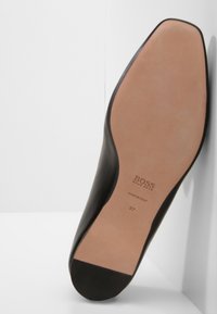 Černá kožená bota s špičatou špičkou a minimalistickým designem. Obsahuje béžovou koženou podrážku s označením značky a velikosti.