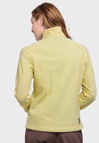 Fleecejacke in hellgelb mit hohem Kragen, ausgestattet mit kontrastierenden Nähten und einem runden Logodetail auf dem unteren Rücken.