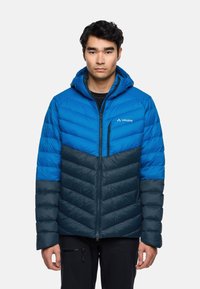 Giacca isolante blu e grigio scuro con cappuccio. Presenta un motivo a zigzag, tasca sul petto con zip e polsini elasticizzati. Design leggero.