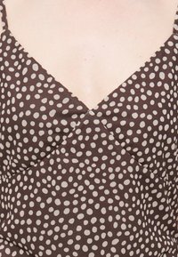 Καφέ φόρεμα με ακανόνιστες ανοιχτό μπεζ πουά, λεπτές τιράντες και V-λαιμόκοψη σε γυμνό δέρμα.