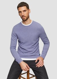  Lichtpaarse textuurtrui met lange mouwen en een ribbelrand, gedragen over een wit T-shirt met ronde hals. Gecombineerd met donkere spijkerbroek.