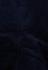 Gros plan d’un tissu en velours côtelé bleu foncé montrant des côtes verticales et une texture pliée.