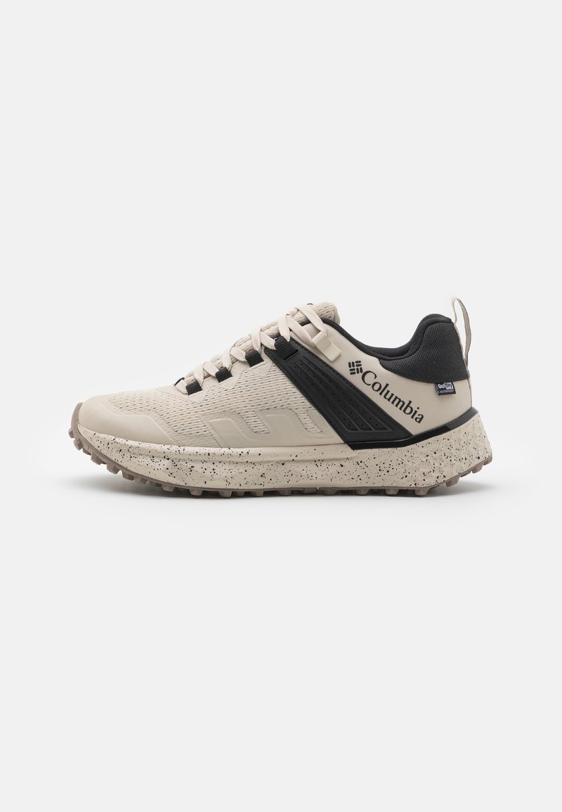 Columbia sneakers in beige and black, with a textured mesh upper, speckled midsole, and durable rubber outsole for traction.