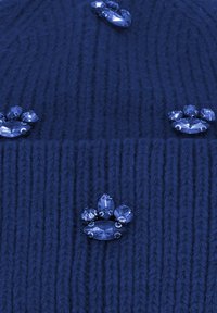 Cappello di lana blu navy con quattro gemme trasparenti incastonate a forma di zampa. Il design testurizzato presenta una lavorazione a coste verticali.