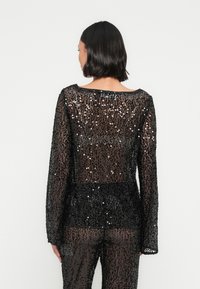 Haut noir à sequins avec manches longues, encolure dégagée et texture transparente, présentant une silhouette ajustée et des ornements brillants sur toute la surface.