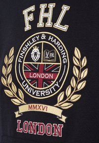 Schwarzer Stoff mit einem bestickten runden Emblem. Details umfassen einen Löwen, Farben der britischen Flagge, einen goldenen Lorbeerkranz und den Text "FHL LONDON".