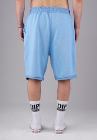 Light blue cotton shorts with a relaxed fit, elastic waistband, and rolled hems. Worn with white socks featuring black lettering and sneakers.