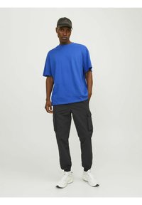 Blå bomuld t-shirt med korte ærmer, parret med sorte cargo bukser med sidelommer og hvide sports sneakers.