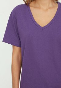 T-shirt violet en V fabriqué en coton doux avec des manches courtes. Coutures plates et coupe décontractée, mettant en valeur une texture lisse et uniforme.