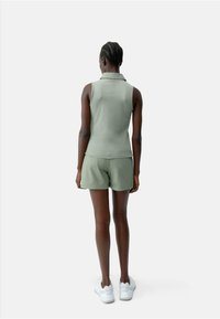 Olijfgroene mouwloze poloshirt met bijpassende shorts, met een gladde textuur. Gecombineerd met witte sneakers; achteraanzicht.