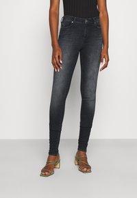Jeans ajustados de denim oscuro con una textura suave, que cuentan con cinco bolsillos, un cierre de cremallera y botón, y detalles de desvanecimiento sutil en las piernas.