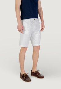 Shorts en coton blancs avec une texture lisse, longueur genou, coupe droite, fermeture par un seul bouton, associés à des chaussures de pont marron.