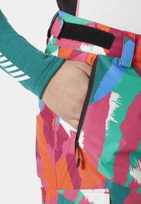 Pantalones de esquí coloridos con estampados que presentan trazos audaces en rosa, verde y naranja, con un bolsillo con cremallera y un cierre de velcro.