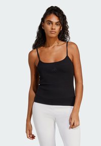 Čierny rebrovaný tielko s tenkými ramienkami a srdcovým výstrihom; má jemné logo na hrudi; doplnené bielymi legínami.