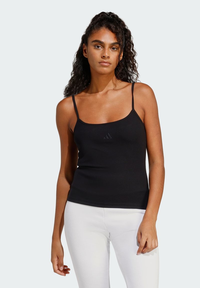 Čierny rebrovaný tielko s tenkými ramienkami a srdcovým výstrihom; má jemné logo na hrudi; doplnené bielymi legínami.