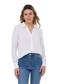 Camicia bianca a maniche lunghe con colletto, chiusura con bottoni frontale e texture morbida, abbinata a jeans in denim blu. Design chiaro e semplice.