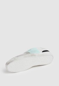 Sneaker bianco con suola in gomma testurizzata, caratterizzato da accenti blu chiaro e neri, e sovrapposizioni in suede. Il design include più texture sui pannelli.