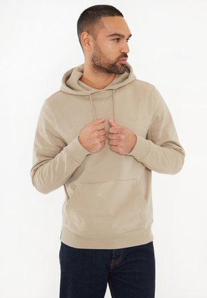 Felpa beige con cappuccio e tasca a marsupio, polsini e orlo a costine. Materiale morbido con una texture liscia, indossata sopra jeans scuri.