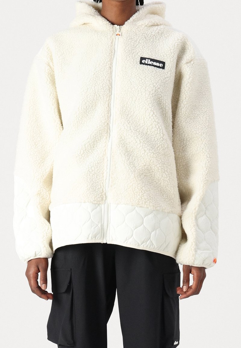 Veste à capuche en polaire crème avec une fermeture zippée, dotée d'une partie inférieure matelassée et d'un petit patch logo noir sur la poitrine.