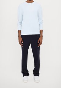 Jasnoniebieski dzianinowy sweter z długimi rękawami i okrągłym dekoltem, zestawiony z ciemnogranatowymi spodniami i białymi trampkami. Miękka faktura i luźny krój.