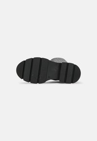 Černá gumová podrážka boty s texturovaným vzorem, obsahující drážkované sekce a kruhové body pro trakci pro lepší grip. Placka, robustní a funkční design.