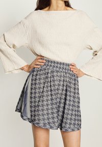 Krémový top s texturou a širokými zvonovými rukávy, spárovaný se sukní s šedým houndstooth vzorem a elastickým pasem.