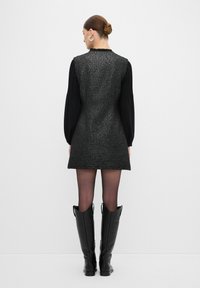 Vestido texturizado negro y plateado con un diseño elegante, complementado con largas mangas negras y botas negras hasta la rodilla.