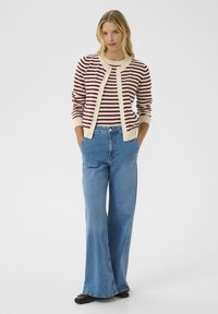 Red and cream striped cardigan with button closures, worn over a blue top and wide-leg blue denim jeans, paired with black shoes.