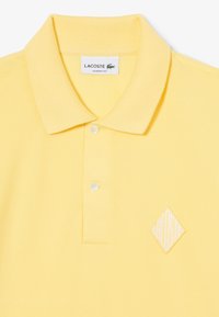 Polo in cotone giallo con colletto a coste, due bottoni e logo ricamato a forma di diamante sul lato sinistro. Tessuto lavorato a trama.