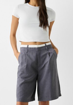 Witte getailleerde crop top gekoppeld aan grijze plooishorts, met een contrasterende witte tailleband en zijzakken. Gladde textuur en op maat gemaakt ontwerp.