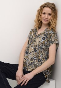 Blusa a maniche corte in verde oliva con motivi floreali e foglie in blu e crema. Presenta un collo a barchetta e una vestibilità ampia e rilassata.