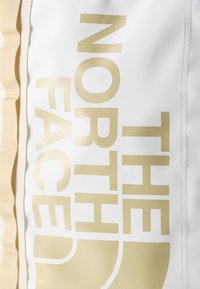 Λευκό ύφασμα με μπεζ υφαντό και το λογότυπο "THE NORTH FACE" τυπωμένο με μεγάλα μπεζ γράμματα.