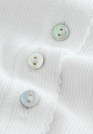 Hvid ribbet stof med tre runde, iriserende knapper med to huller og en dekorativ bølget kant.