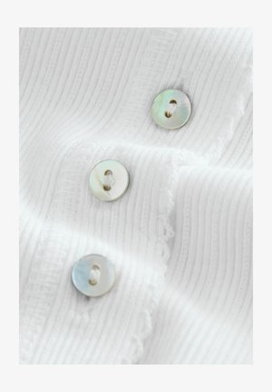 Weißes, geripptes Stoffstück mit drei runden, irisierenden Knöpfen mit zwei Löchern und einem dekorativen, gezackten Rand.