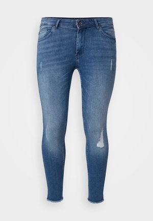 Lieknos džinsai iš mėlynos denim medžiagos, su nusidėvėjimo detalėmis priekyje, išblukusiomis vietomis ir suplėšytu apvadu ties kulkšnimis.